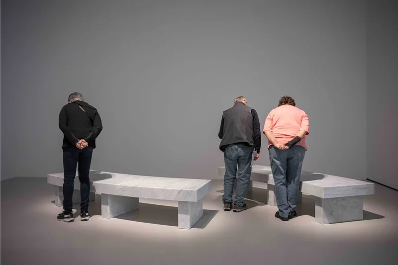 Trois personnes observant des sculptures en marbre en forme de banc