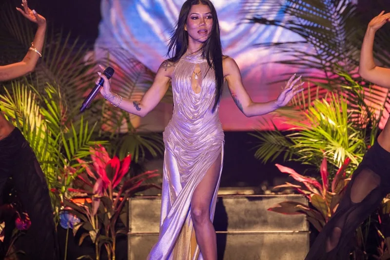 Chanteuse sur scène en robe dorée avec des plantes autour.