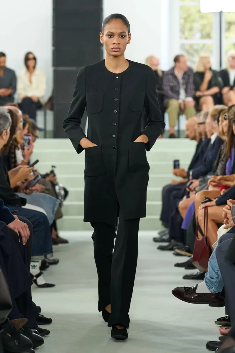 Modèle défilant en ensemble noir lors d'un défilé de mode.