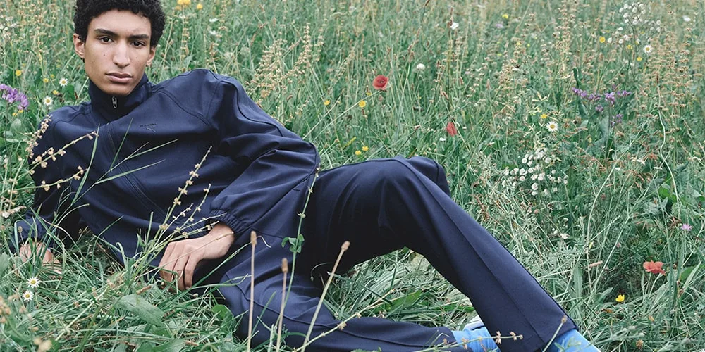 Un homme en tenue sombre est allongé dans un champ de fleurs sauvages.