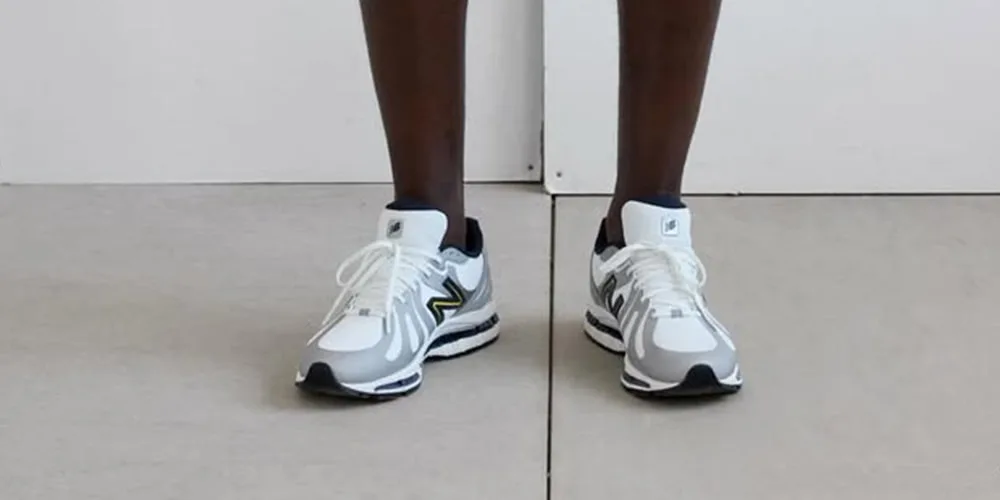 Personne portant des baskets blanches et grises sur un sol.