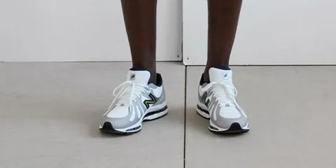 Personne portant des baskets blanches et grises sur un sol.