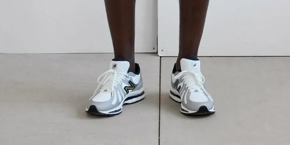 Personne portant des baskets blanches et grises sur un sol.
