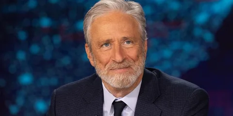 Portrait d’un homme aux cheveux gris en costume devant un fond bleu flou