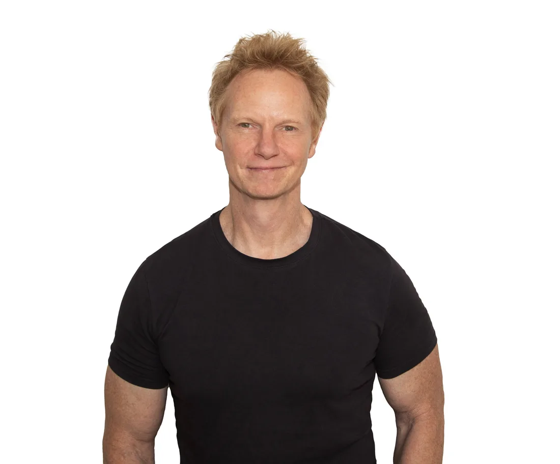 Homme souriant en t-shirt noir sur fond blanc.