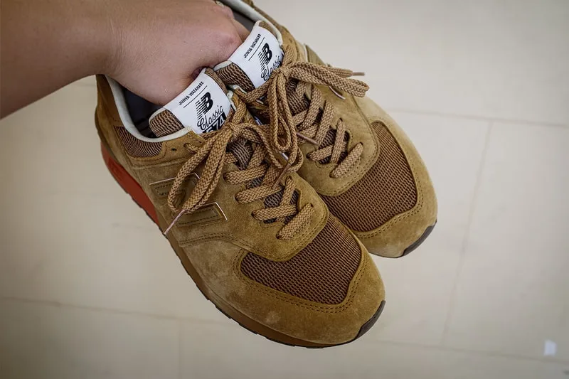 Paire de baskets marron avec logo New Balance tenue à la main.