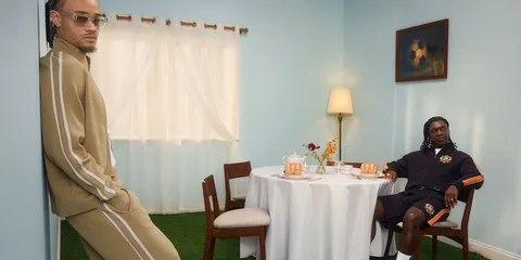 Deux hommes posant dans une pièce avec table et chaise.