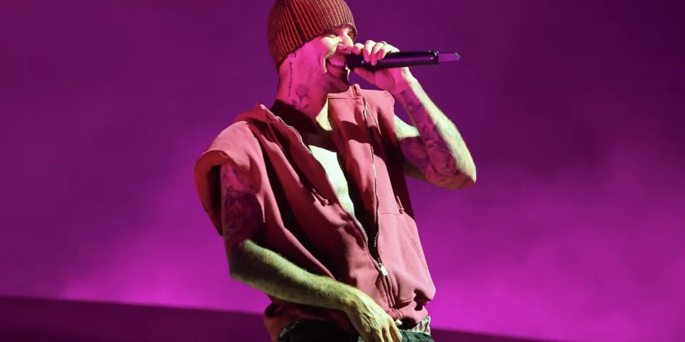 Chanteur avec beanie et microphone sur scène, fond violet.