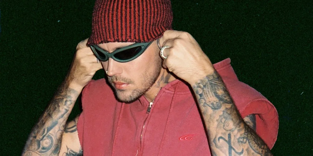 Homme tatoué avec bonnet rouge et lunettes noires, lève le bras.