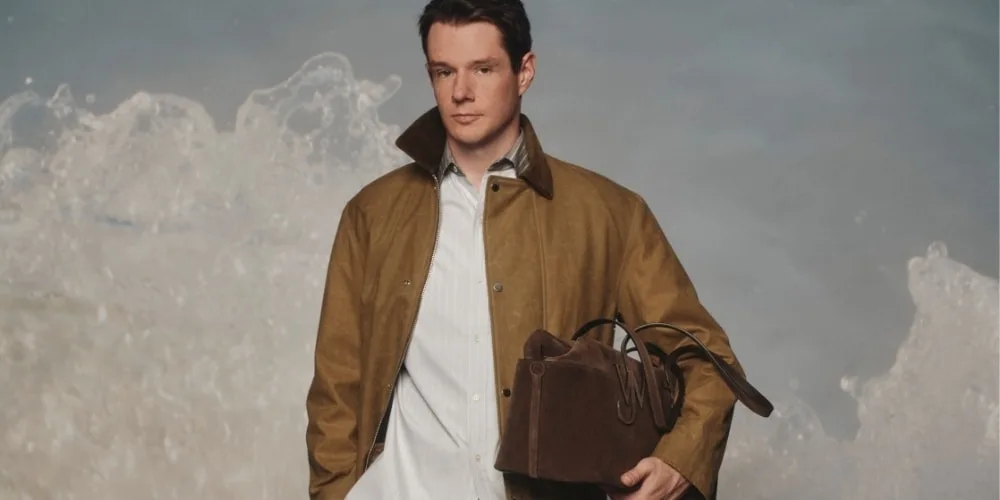 Homme portant un manteau et un sac devant des vagues de mer