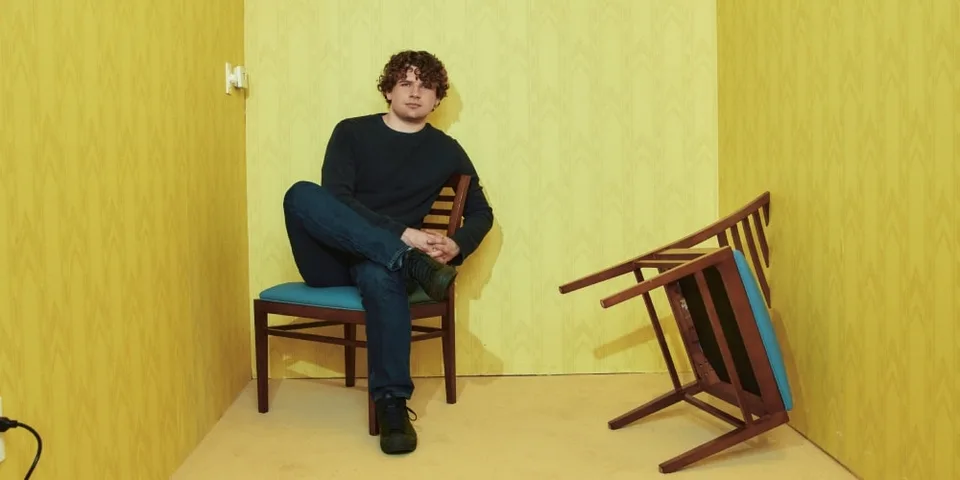 Homme assis sur une chaise dans une pièce jaune, une chaise renversée à côté.
