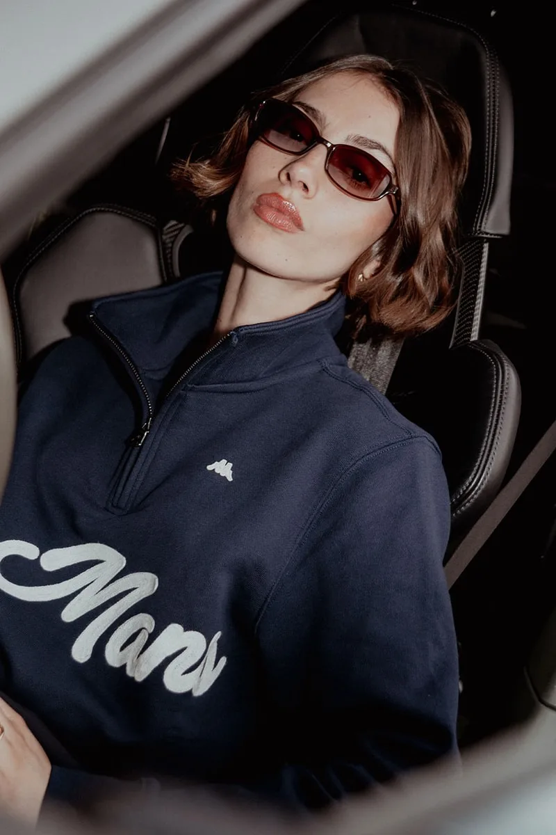 Femme portant des lunettes de soleil et un pull bleu avec 'Mars' brodé.
