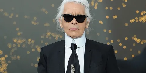 Personne en costume noir avec lunettes de soleil, fond de lumières floues.