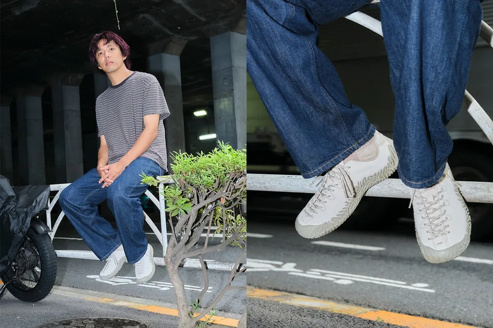 Homme assis sur une barrière en jean et t-shirt rayé, baskets blanches visibles.