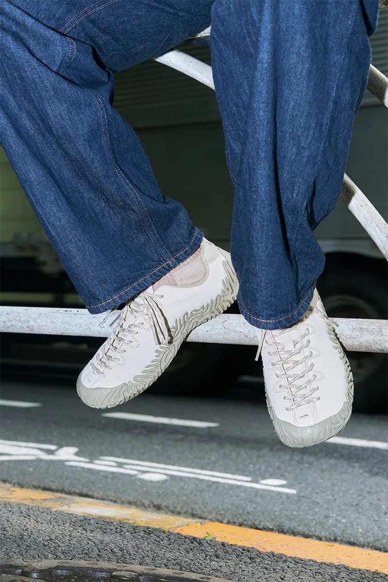 Personne avec jeans et baskets blanches, motif sur la semelle, assis sur une barrière.