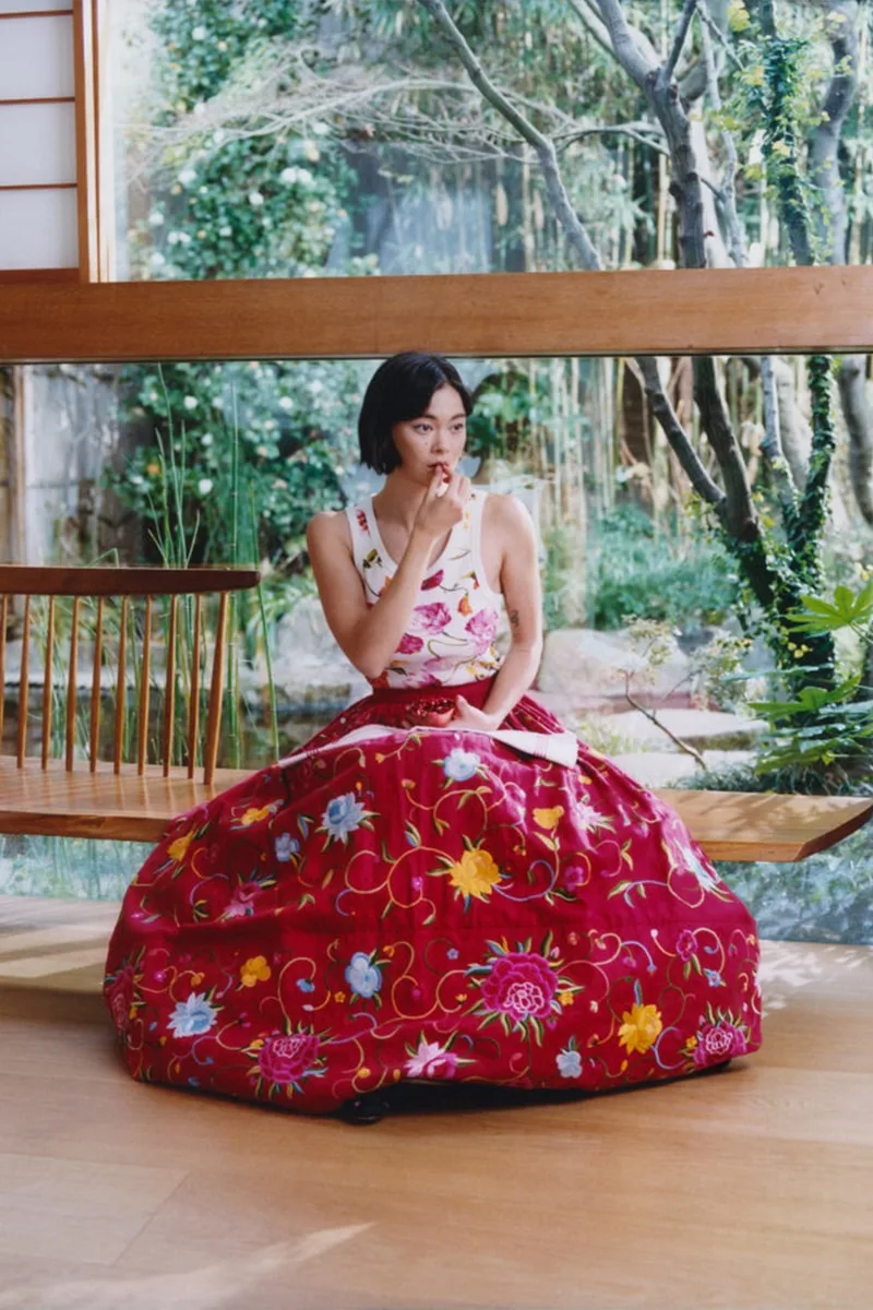 Femme en robe à fleurs rouges assise devant une grande fenêtre.