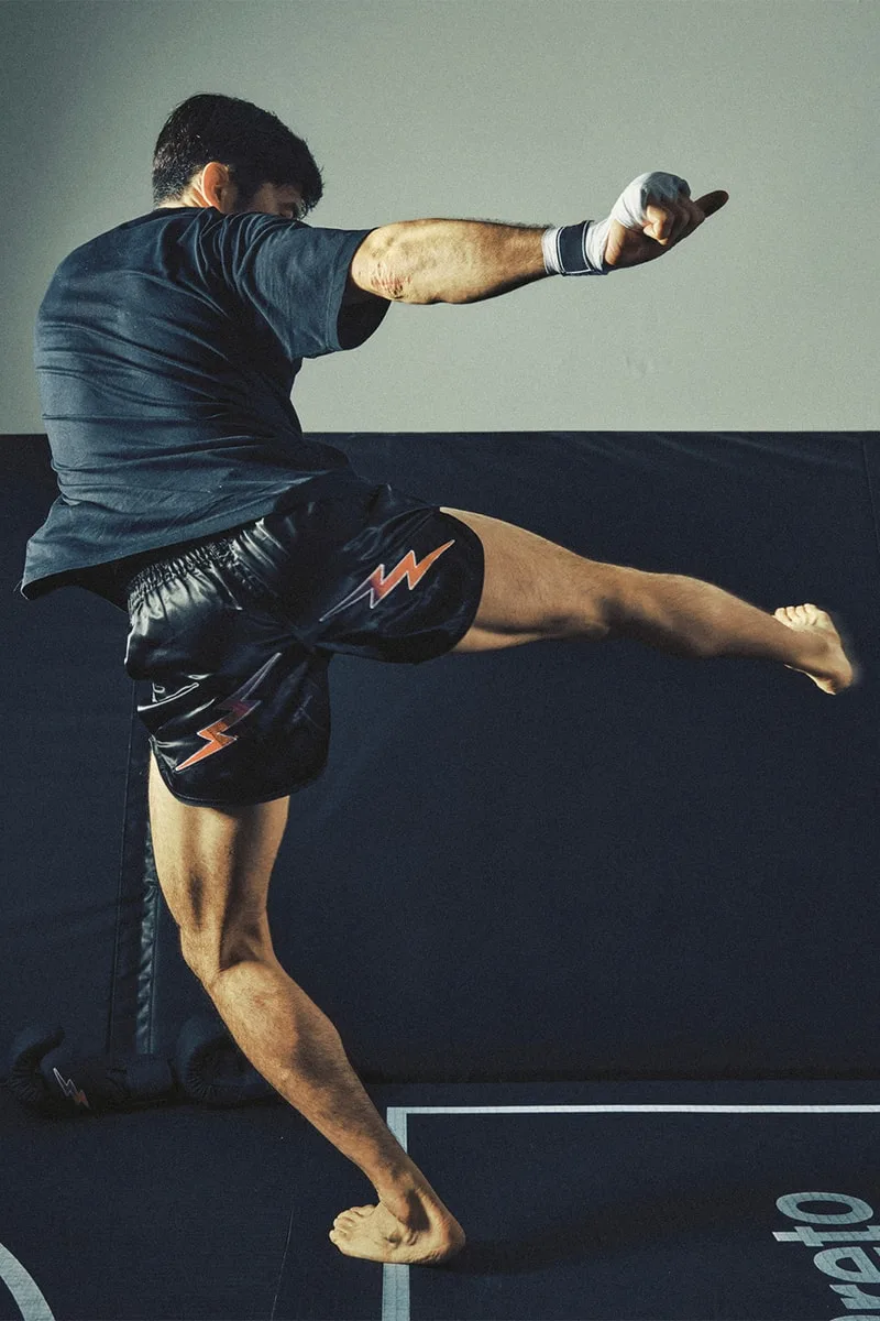 Homme en short et t-shirt frappant avec son pied dans un gymnase de combat.