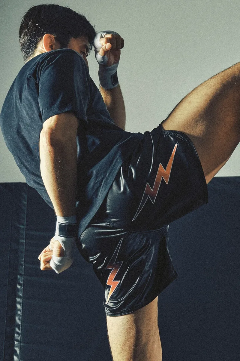 Homme effectuant un coup de pied haut en short noir avec éclair.