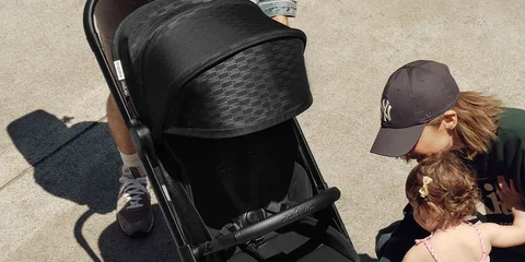 Personnes avec une poussette noire dans un parc ensoleillé.