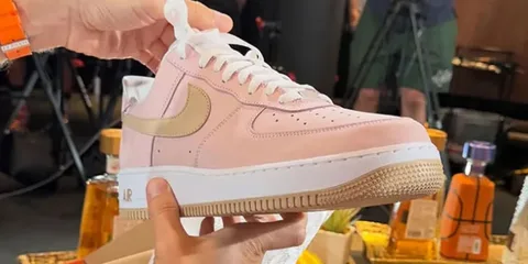 Main tenant une chaussure rose avec logo Nike.