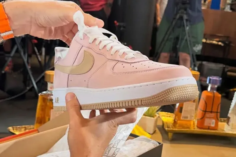 Main tenant une chaussure rose avec logo en fond