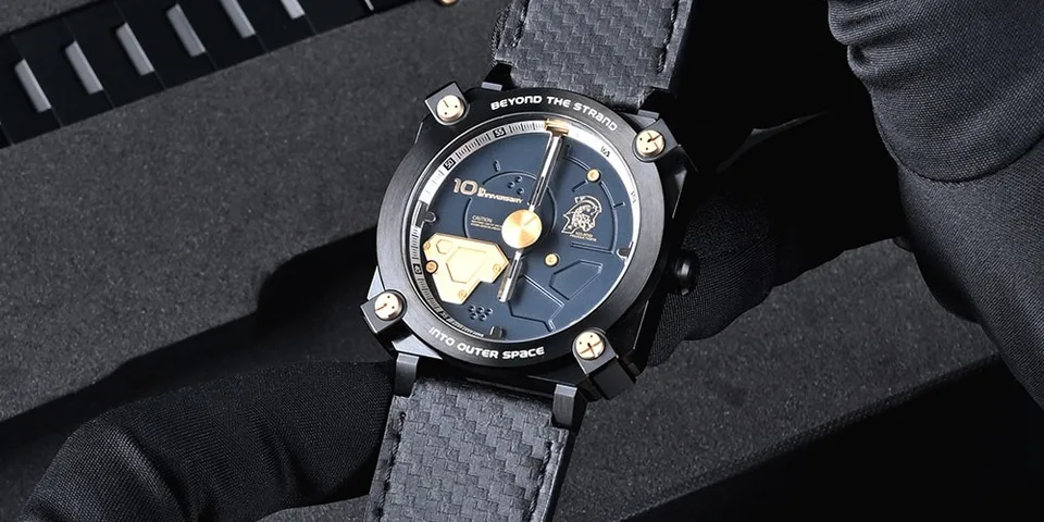 Montre noire avec détails dorés, tenue par une main gantée.