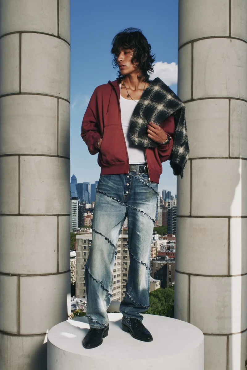 Homme en tenue décontractée, jeans et veste rouge, sur fond de ville.