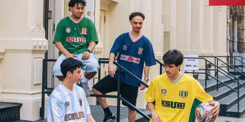 Quatre hommes en maillots de football colorés, assis et discutant dehors.