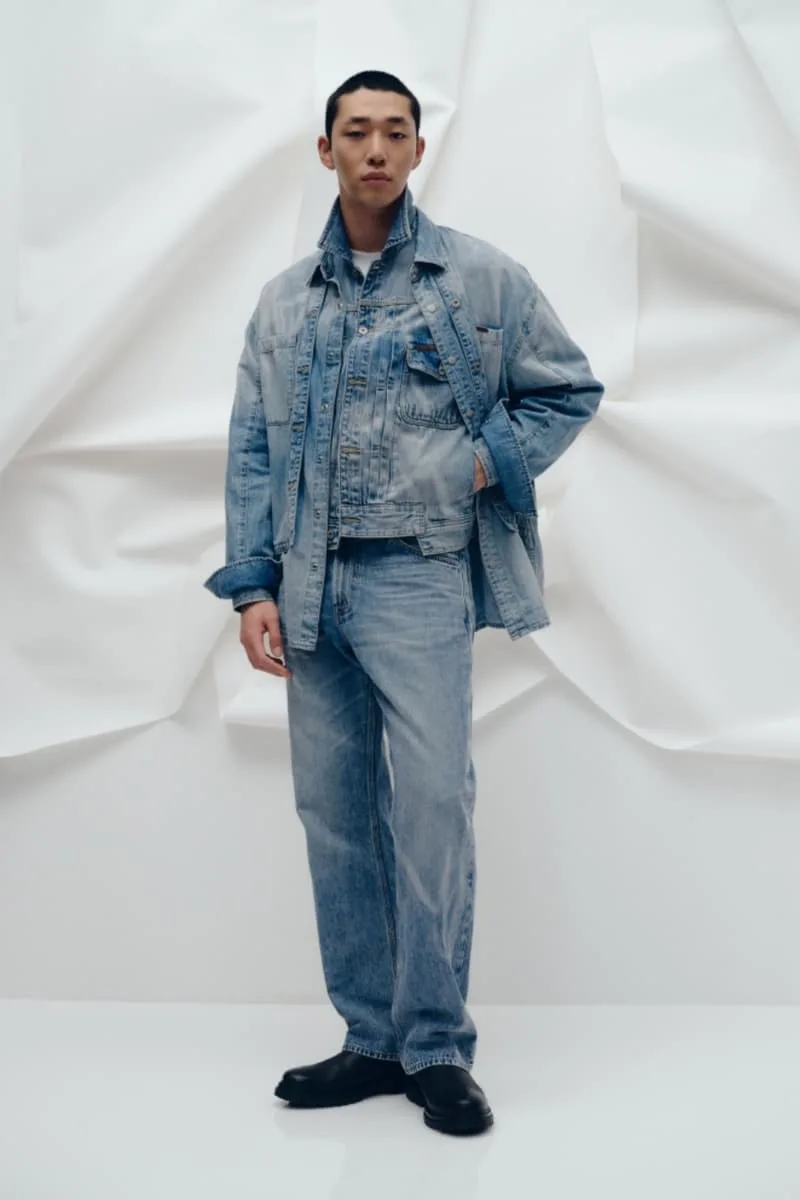 Homme en tenue en jean devant fond blanc texturé.