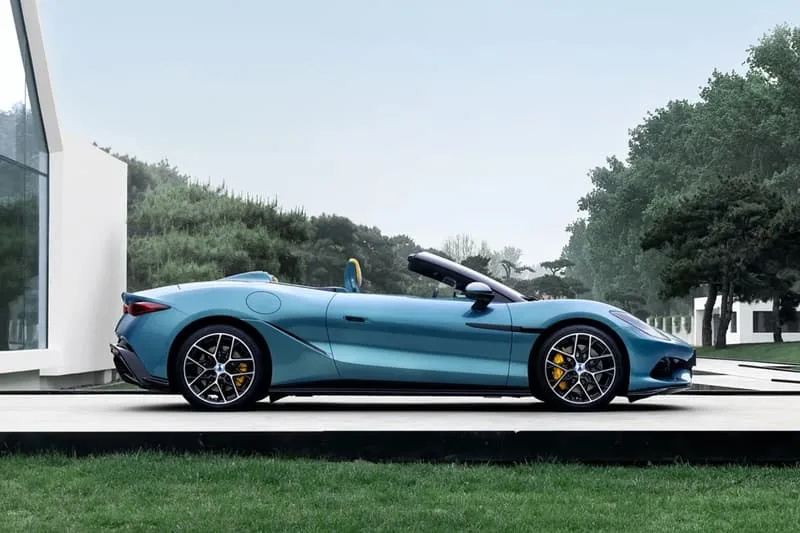 Voiture bleue décapotable garée près d'arbres et d'une maison moderne.