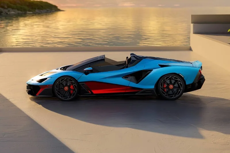 Voiture de sport décapotable bleu et noir près de l'eau au coucher du soleil.