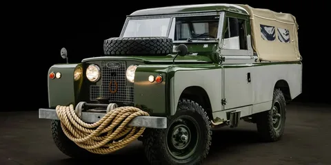Véhicule rétro Land Rover vert et crème avec pneus et corde à l'avant.