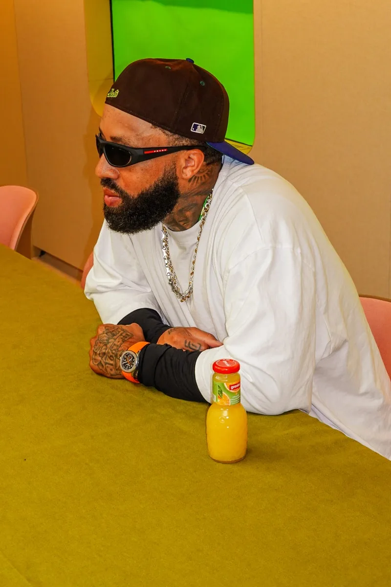 Homme assis avec lunettes de soleil, t-shirt blanc, boisson sur la table.