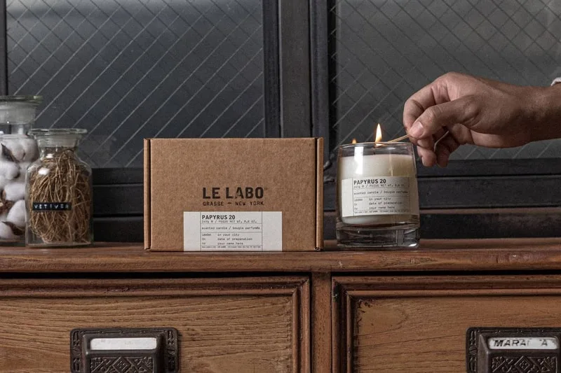 Bougie parfumée Le Labo allumée sur une étagère en bois.