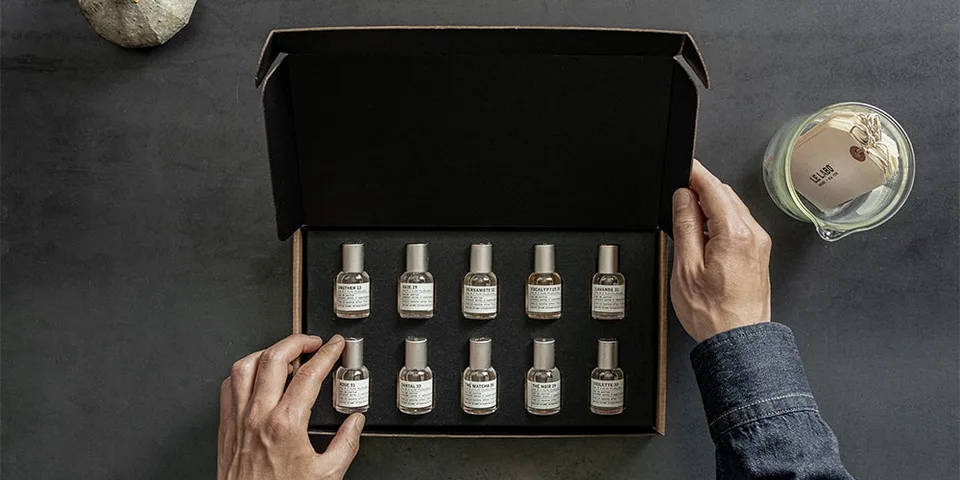 Coffret de parfums miniatures avec bougie sur surface grise.