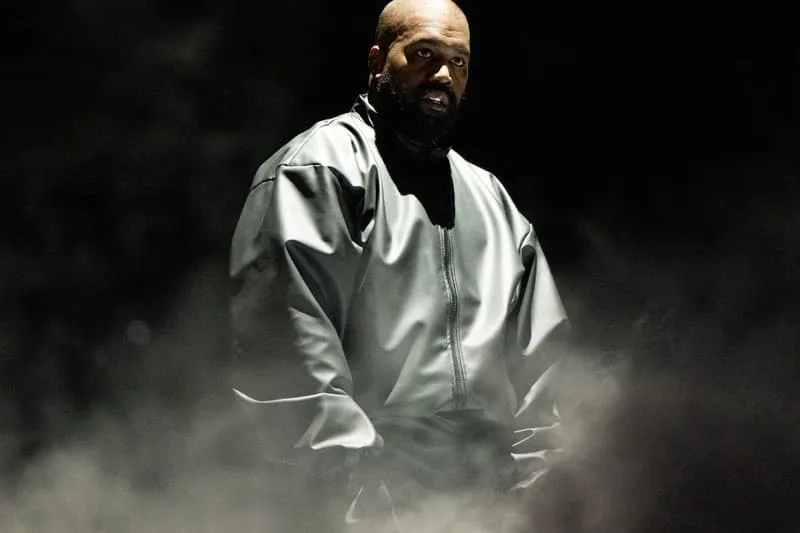 Homme en tenue sombre avec éclairage dramatique et fumée autour.