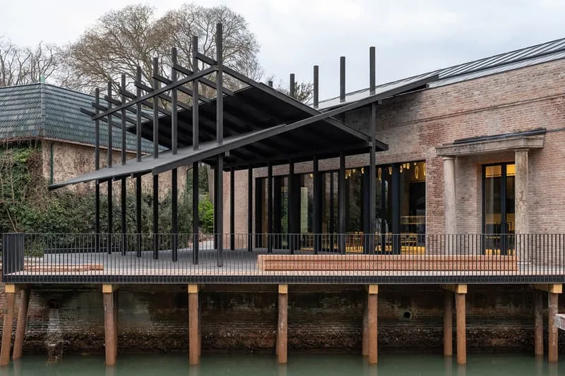 Bâtiment moderne en briques avec terrasse sur pilotis au bord de l'eau.