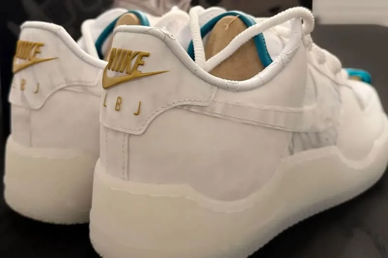 Chaussures blanches avec logo Nike doré et initiales LBJ sur le talon.