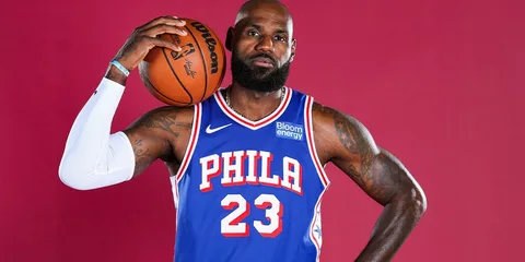 Homme en maillot de basket bleu de Philadelphie tenant un ballon.