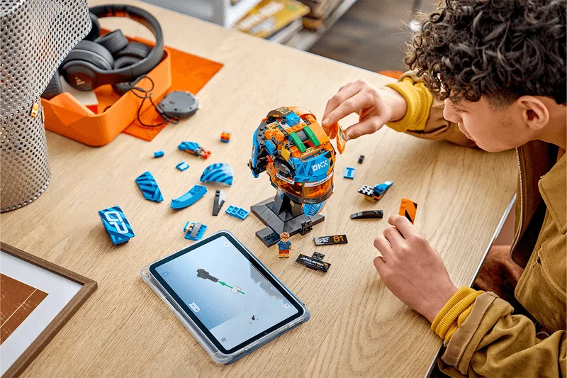 Garçon assemble un casque LEGO coloré avec tablette à proximité.