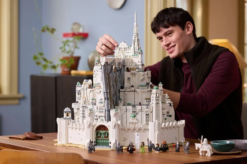 Homme construisant un château LEGO avec des figurines sur une table.