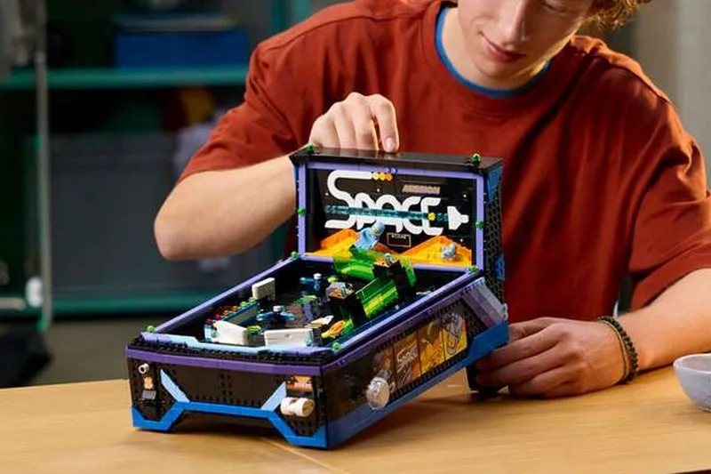 Jeune homme jouant avec un flipper en briques Lego.