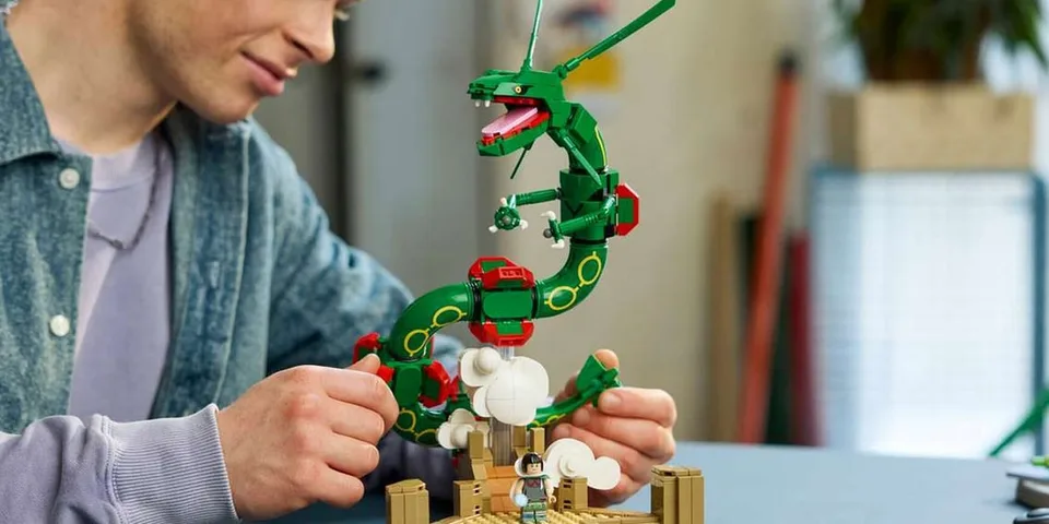 Personne construisant un dragon vert en LEGO sur une table.