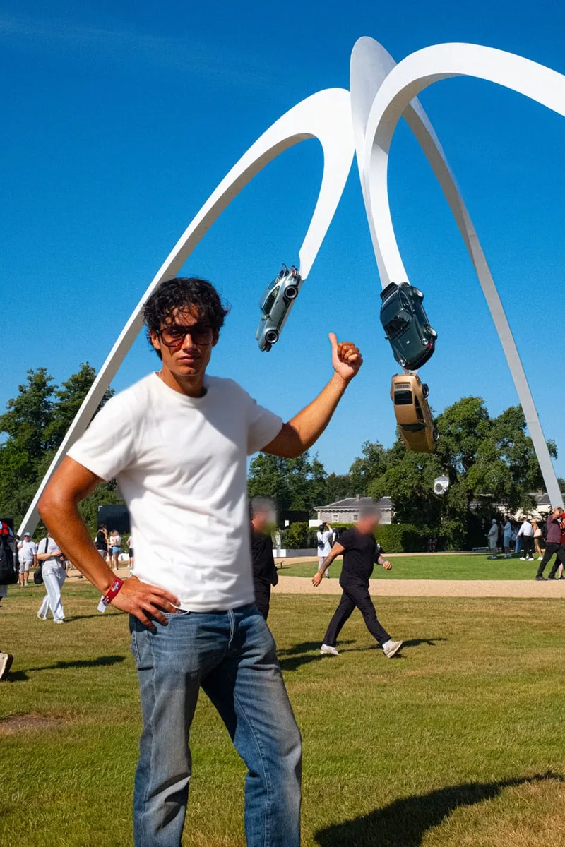Personne posant devant une sculpture de voitures suspendues dans les airs.