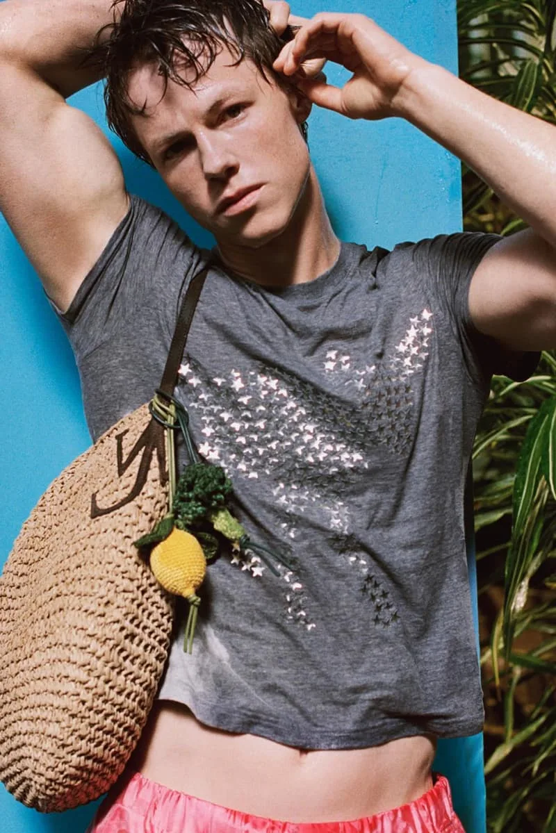Homme en t-shirt gris, sac en paille, fond bleu tropical
