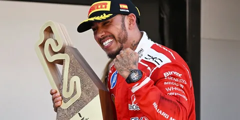 Homme en rouge tenant un trophée et souriant sur un podium.