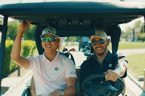 Deux hommes souriants dans une voiturette de golf, sur un parcours ensoleillé.