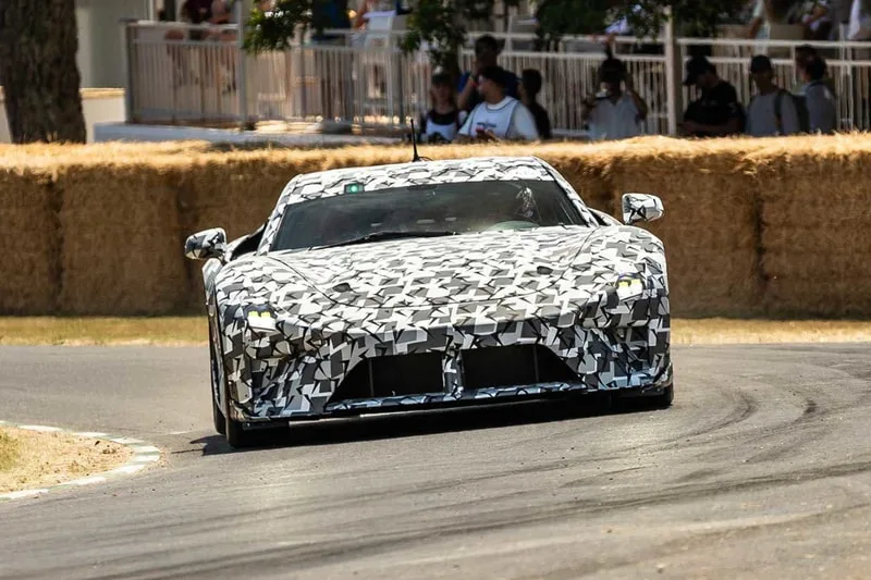 Voiture de sport camouflée sur une piste avec spectateurs en arrière-plan.