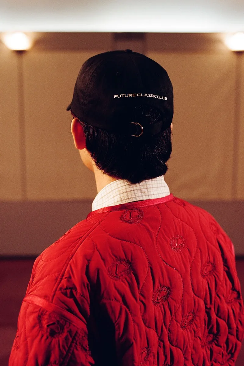 Personne en veste rouge avec casquette noire 'Future Classic Club' dos à la caméra.