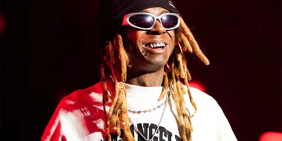 Personne avec des lunettes de soleil et dreadlocks souriant sur scène.